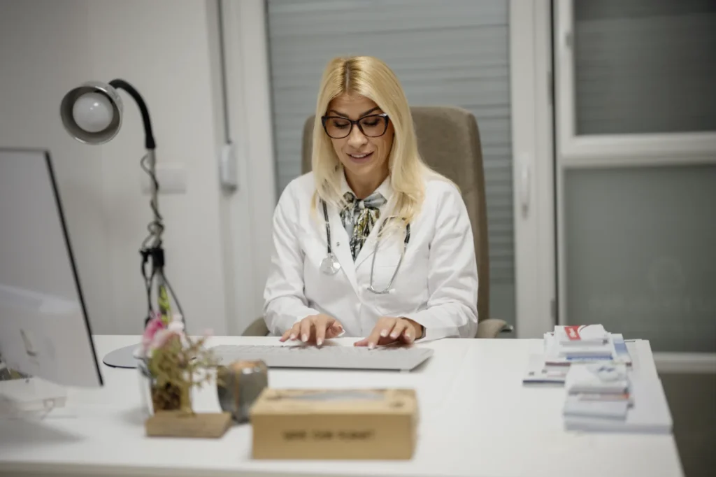 Médica tomando notas en su ordenador durante una consulta con un paciente