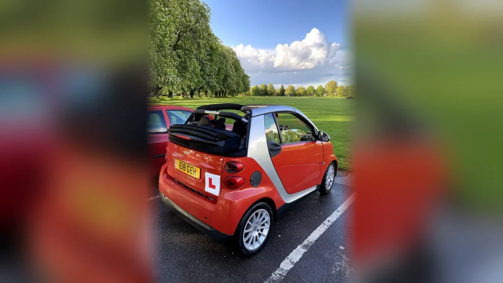 Coche de aprendizaje con placa L de conductor novel aparcado en un parque