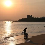 Padre e hijo paseando por la orilla del mar al atardecer, imagen ilustrativa de un seguro de vida familiar